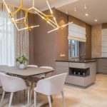 Contemporary open plan kitchen with gray matte cabinets and dining table under contemporary geometric lamp in spacous apartment