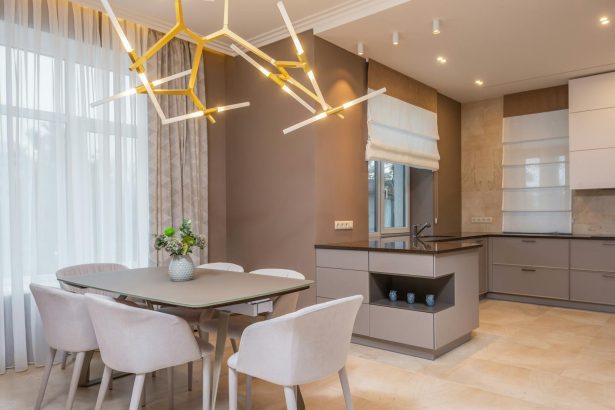 Contemporary open plan kitchen with gray matte cabinets and dining table under contemporary geometric lamp in spacous apartment